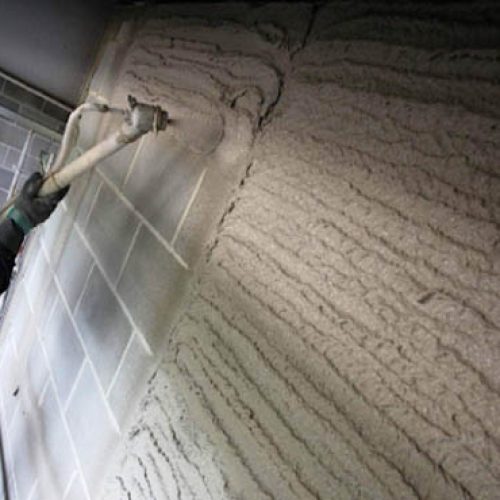 Worker applying cement plaster on wall using spray plastering machine