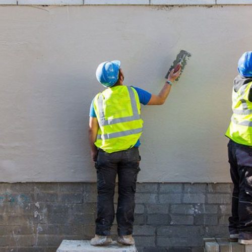 Workers applying cement plaster on exterior brick wall for smooth finish