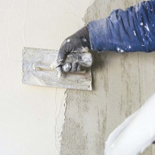 Worker applying wall putty on interior wall using putty knife